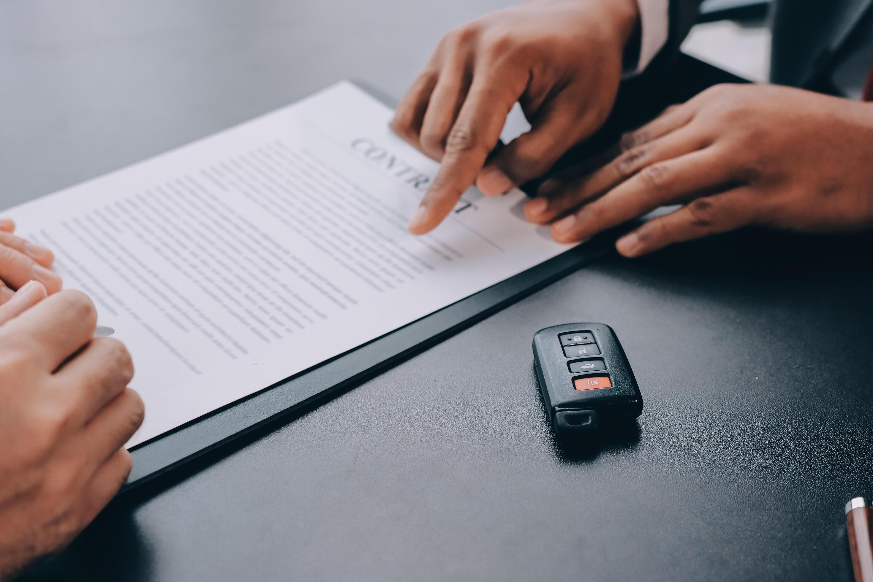 A car buyer and advisor reviewing a vehicle purchase contract beside a key fob